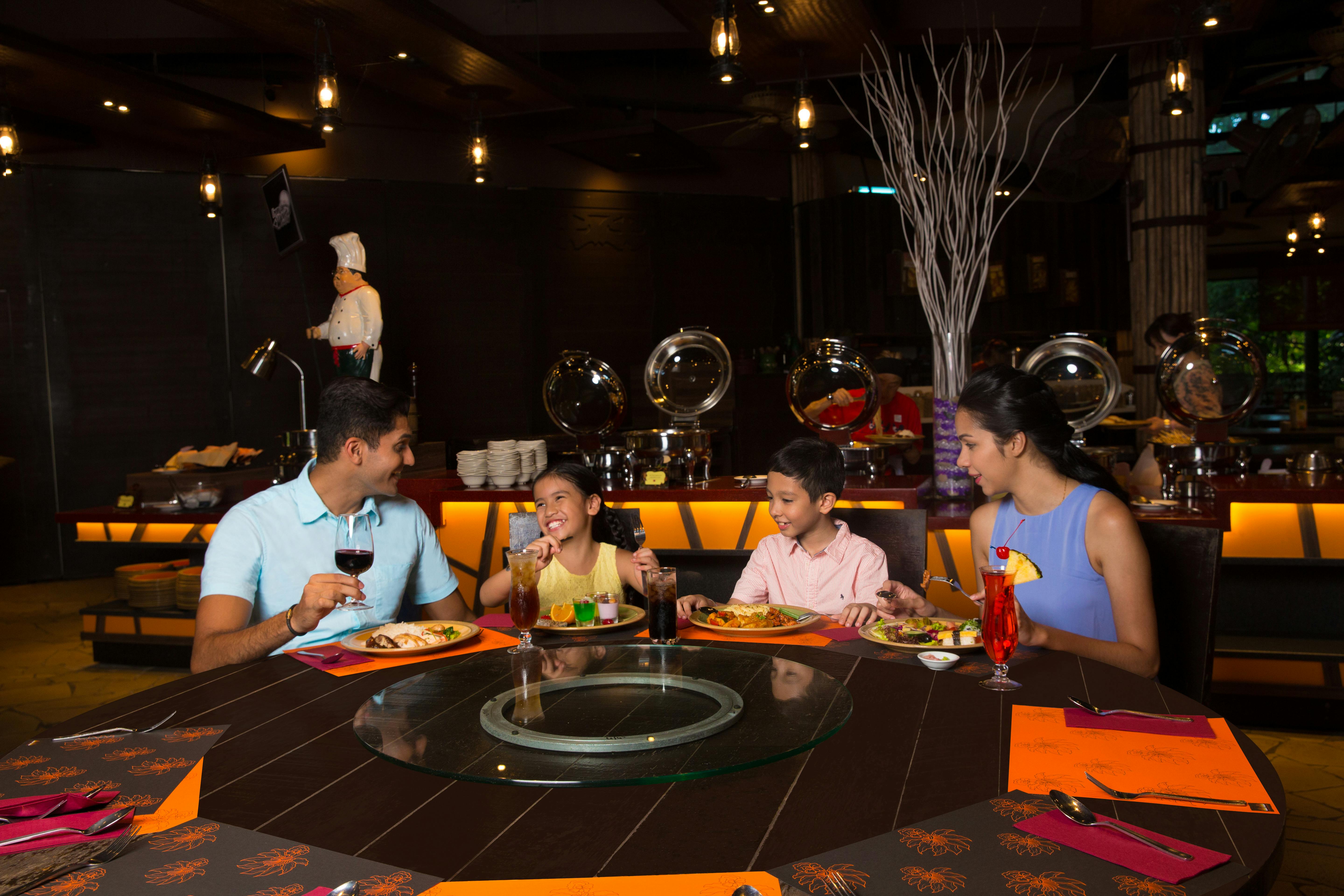 Čtyřčlenná rodina večeří v restauraci a vychutnává si společné jídlo u stolu s oranžovým prostíráním a nápoji.
