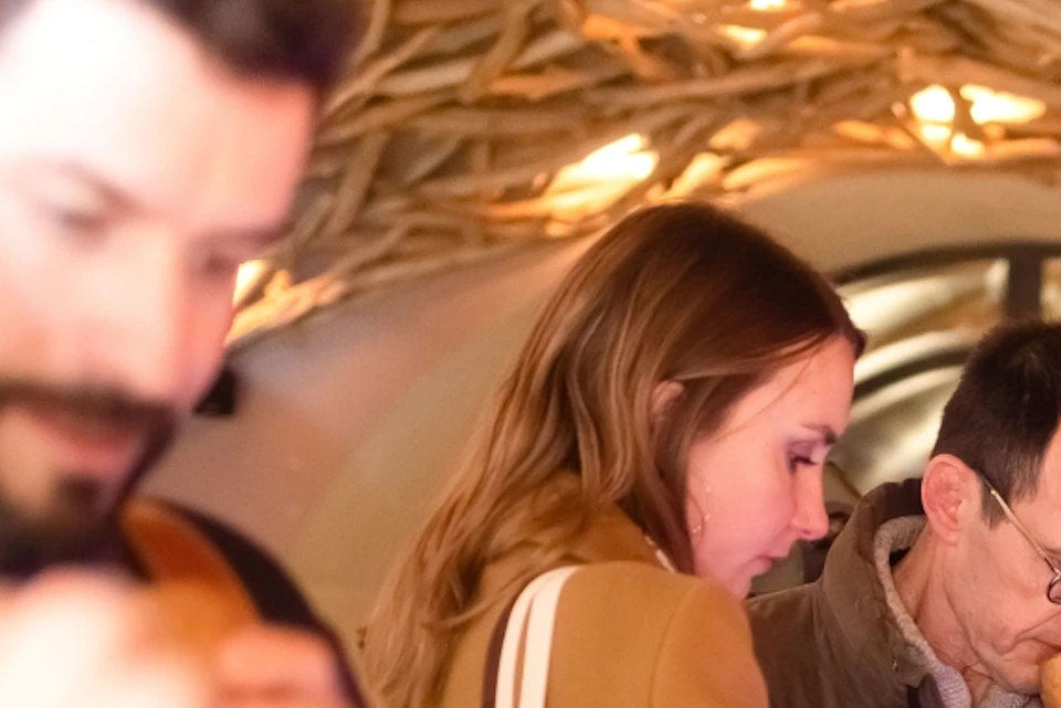 People standing in a line under a wooden arch, holding objects to their noses, possibly engaging in a sensory activity.