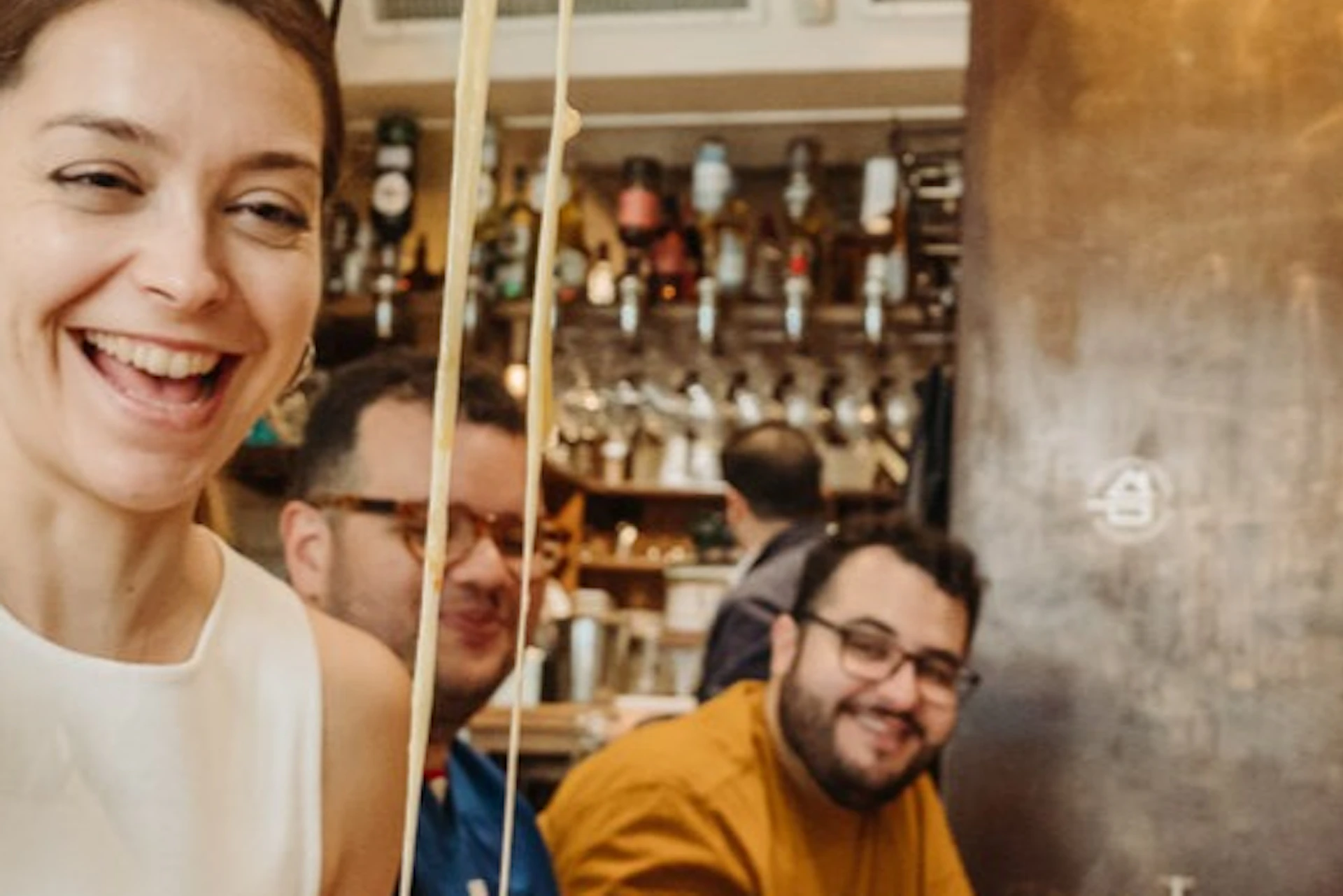A person pulling melted cheese from a dish with a group of people sitting at a table in a cozy restaurant setting.