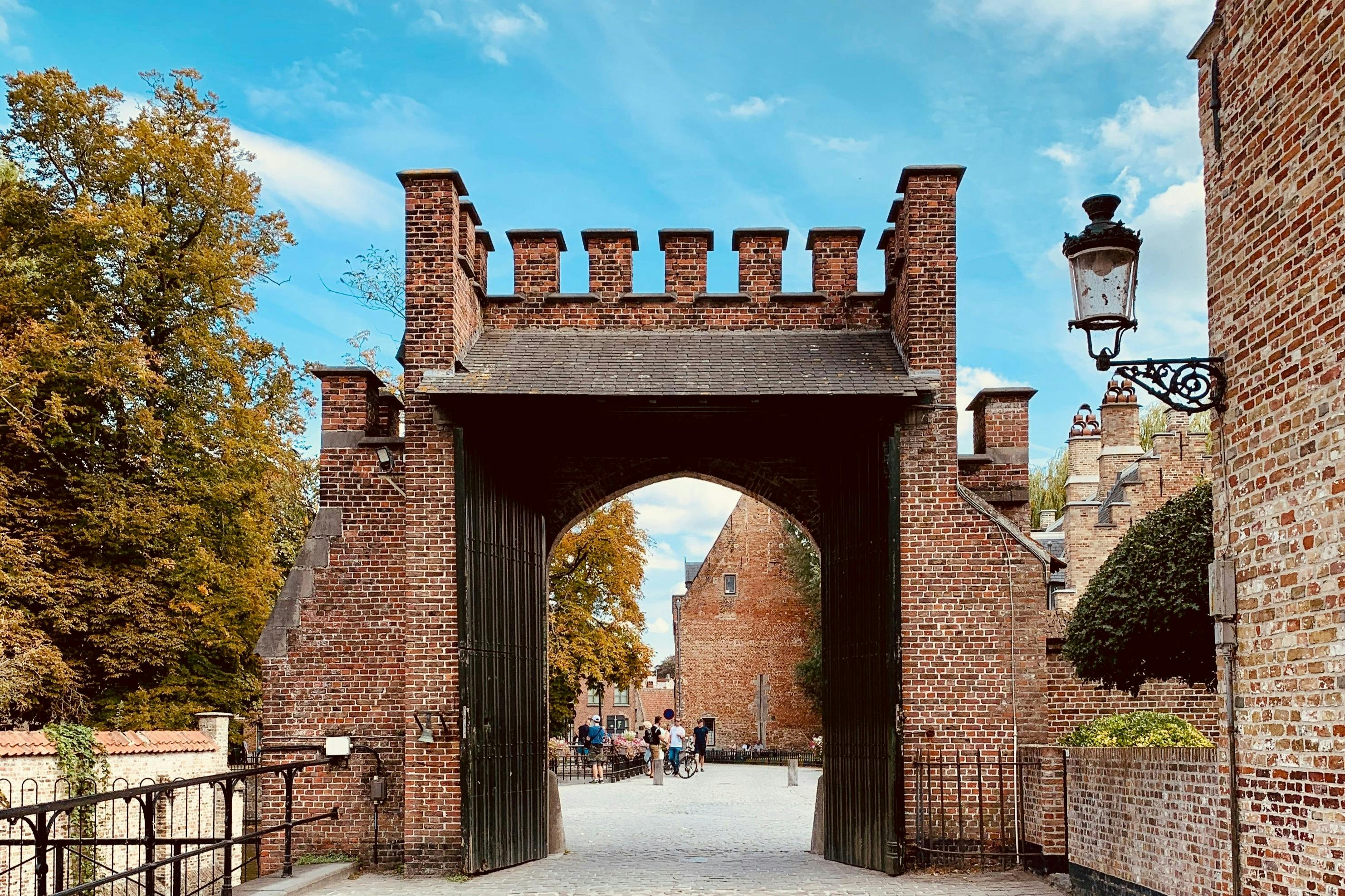 Арка кирпичных замковых ворот с людьми, идущими на заднем плане под голубым небом.