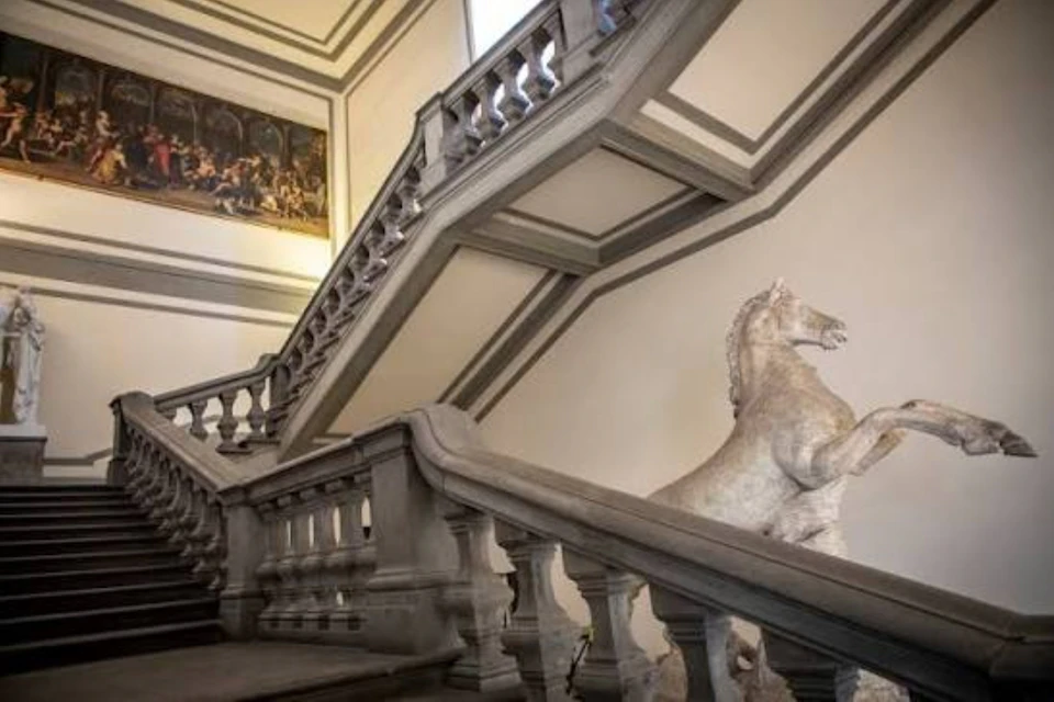 A grand staircase with ornate railings and a statue of a rearing horse in a classical interior space.