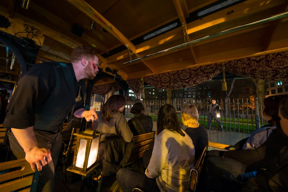 People on a tour bus listen to a guide holding a lantern, while another guide outside speaks, also holding a lantern.