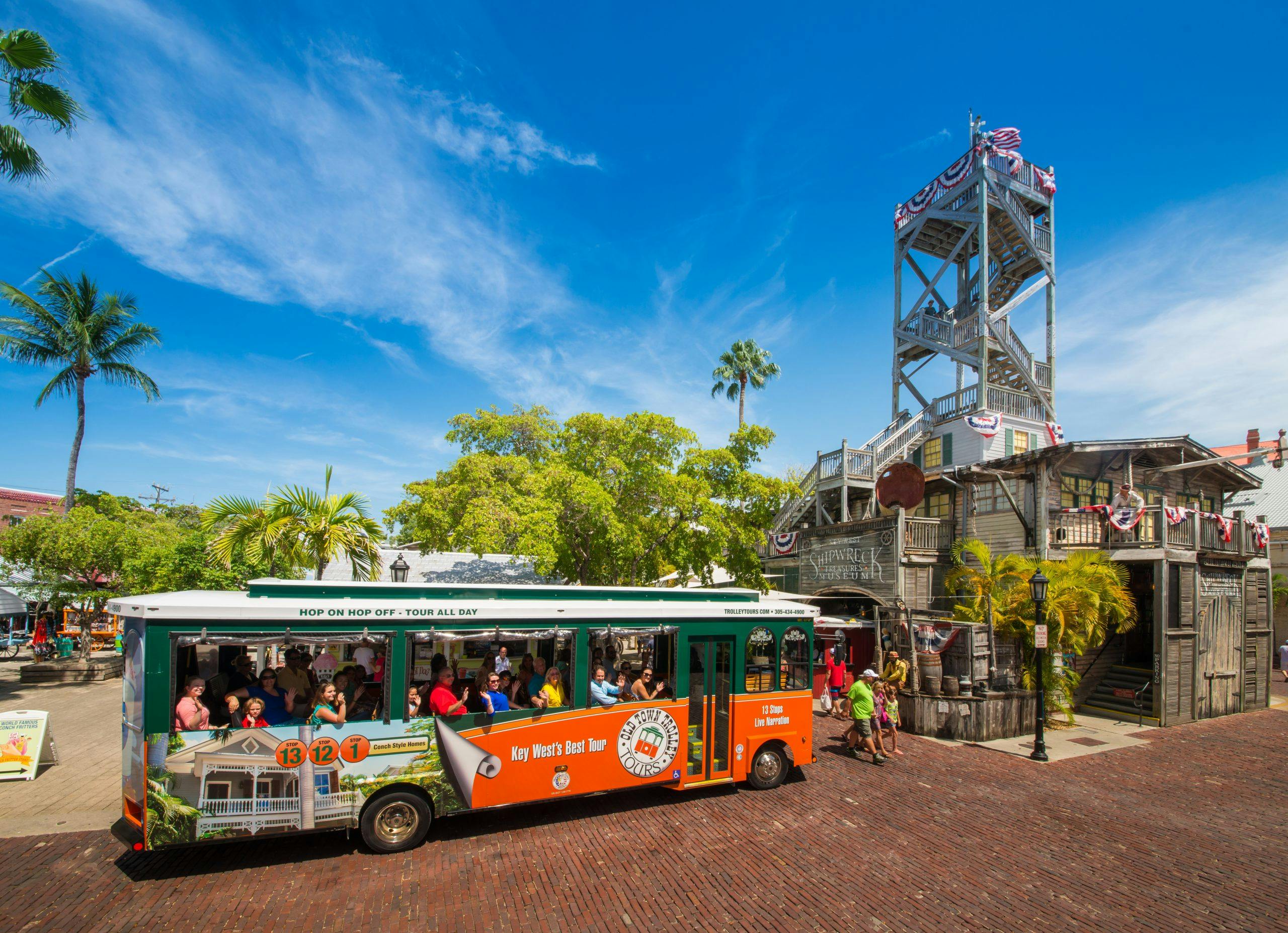 Prohlídkový autobus s lidmi sedícími u dřevěné rozhledny a svěžích zelených stromů pod jasně modrou oblohou.