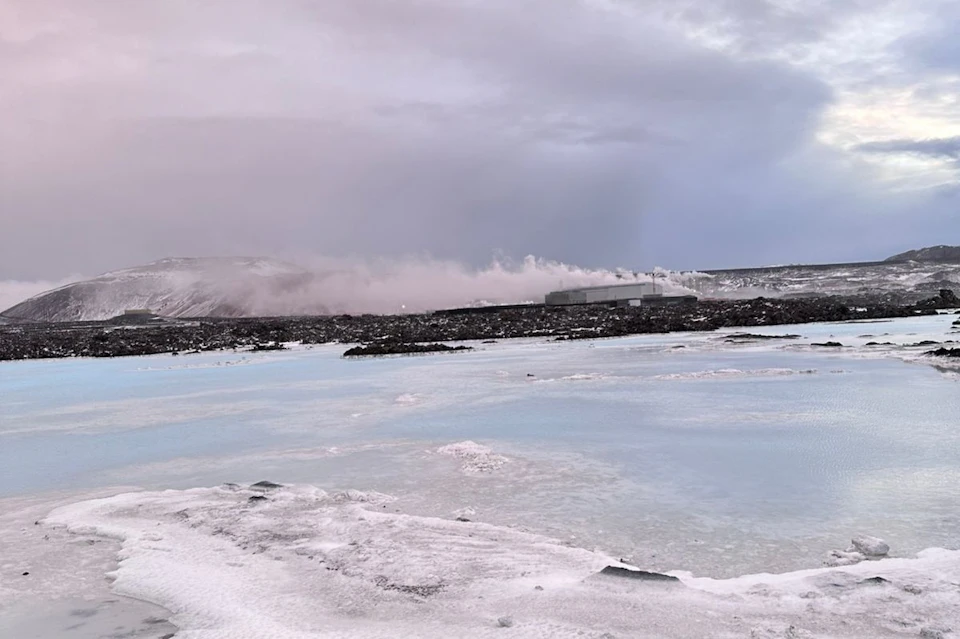 A snowy landscape with a steaming geothermal plant in the distance, under an overcast sky.