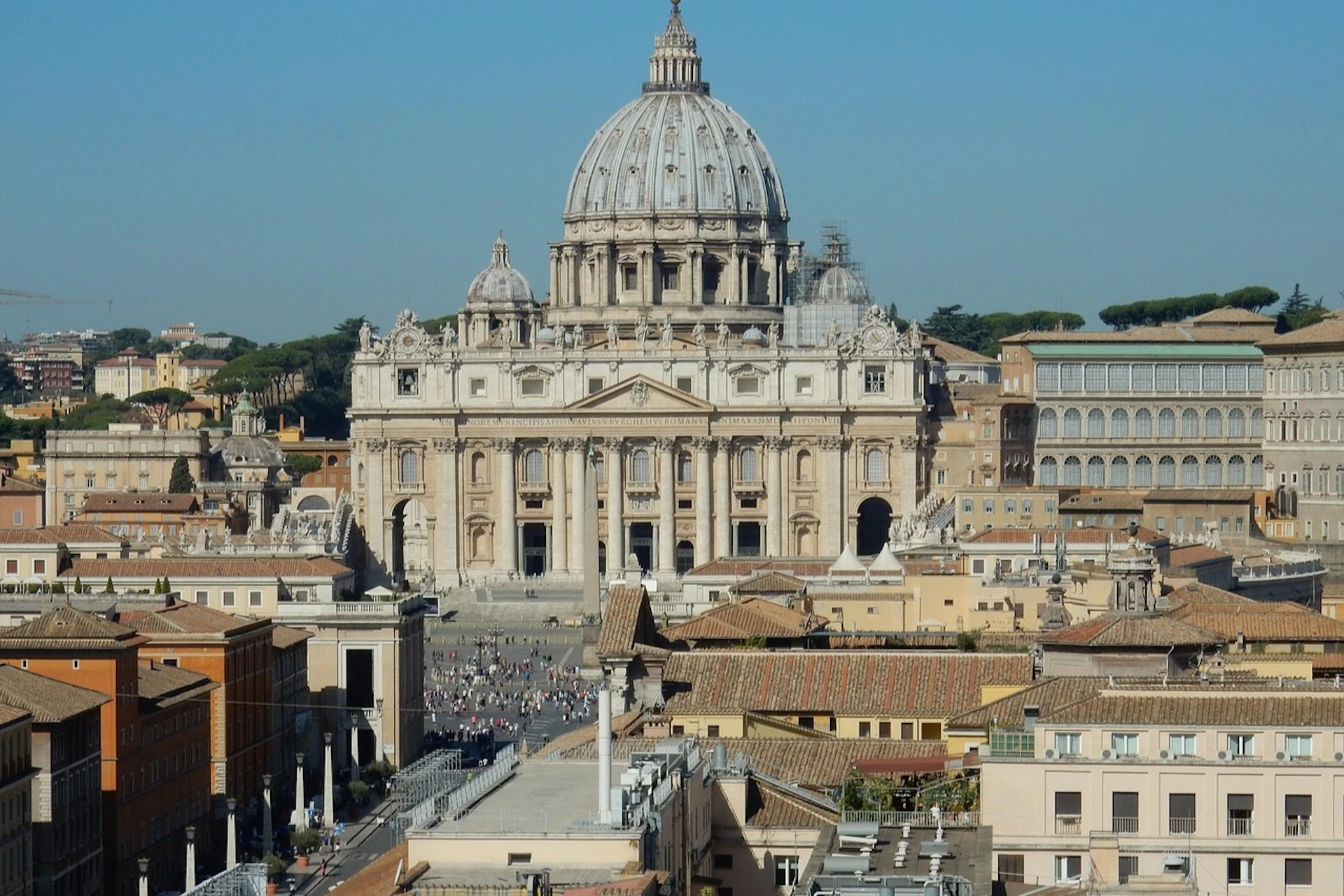 A view of St. Peter's Basilica in Vatican City, with its dome and surrounding buildings under a clear blue sky.