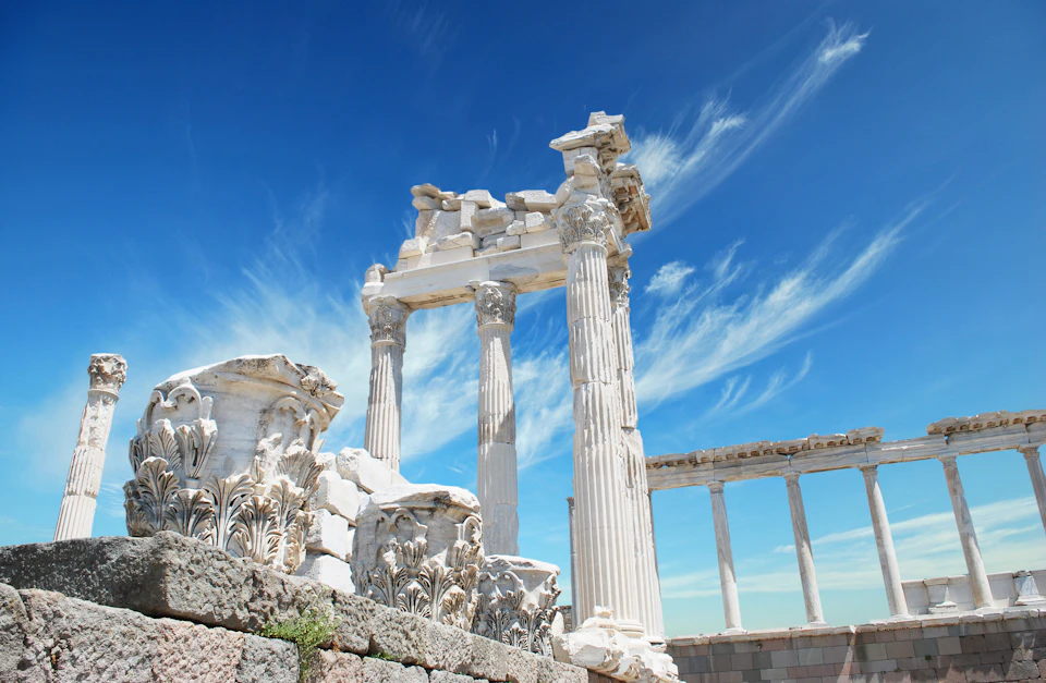 Ancient Greek ruins with tall, white marble columns under a bright blue sky with wispy clouds.