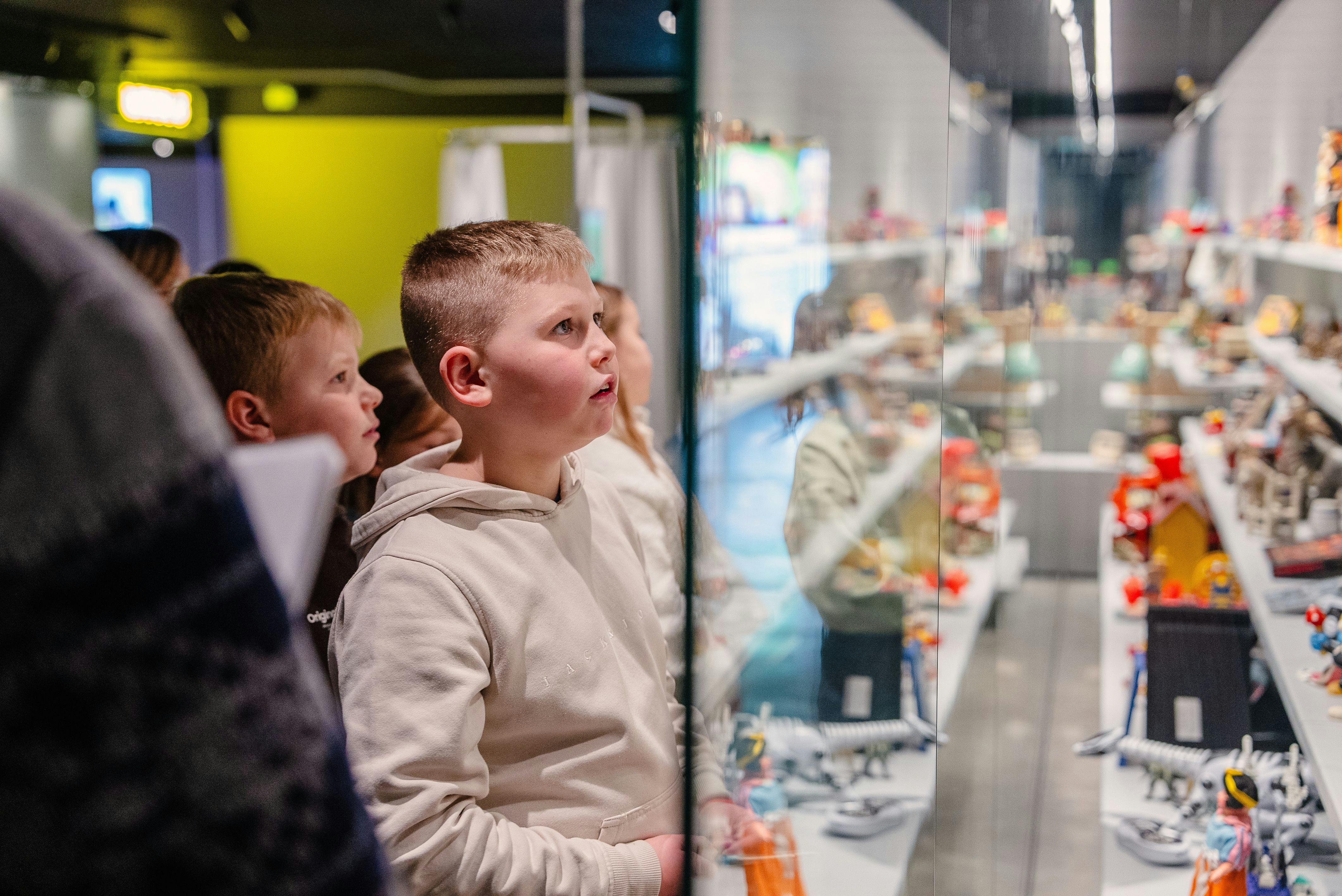Els nens amb caputxa observen atentament una exposició en una exposició interior ben il·luminada, envoltats de gent.