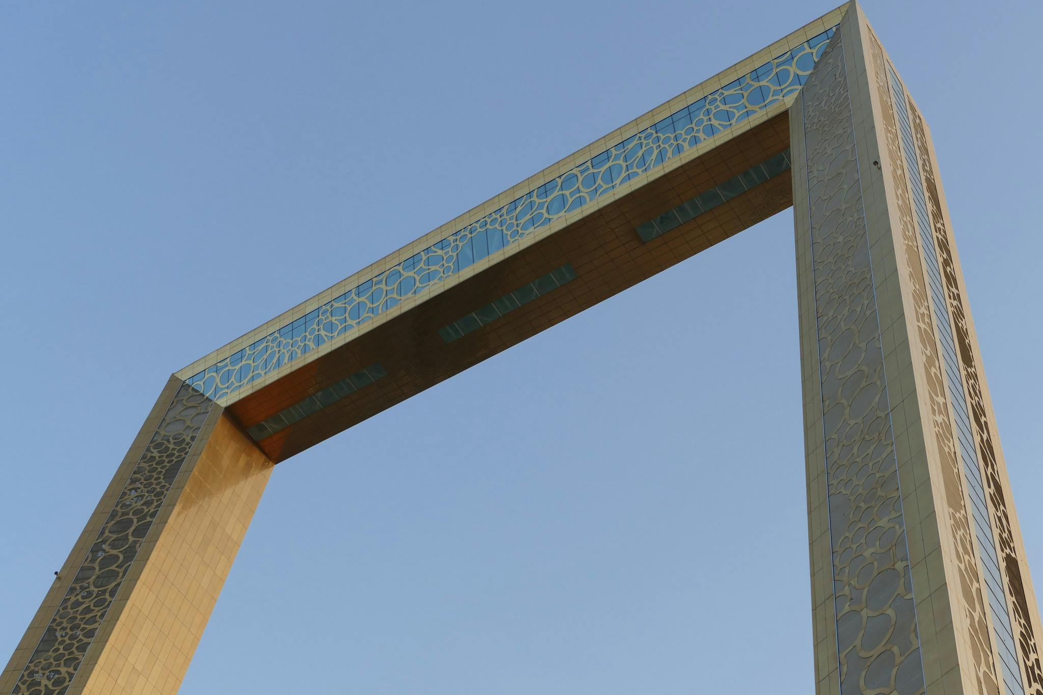 A large rectangular frame structure with intricate patterns, captured against a clear blue sky.