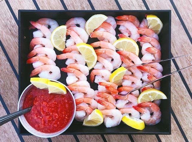 Una safata de gambes amb rodanxes de llimona servida amb un bol de salsa vermella, col·locada sobre una taula de fusta.