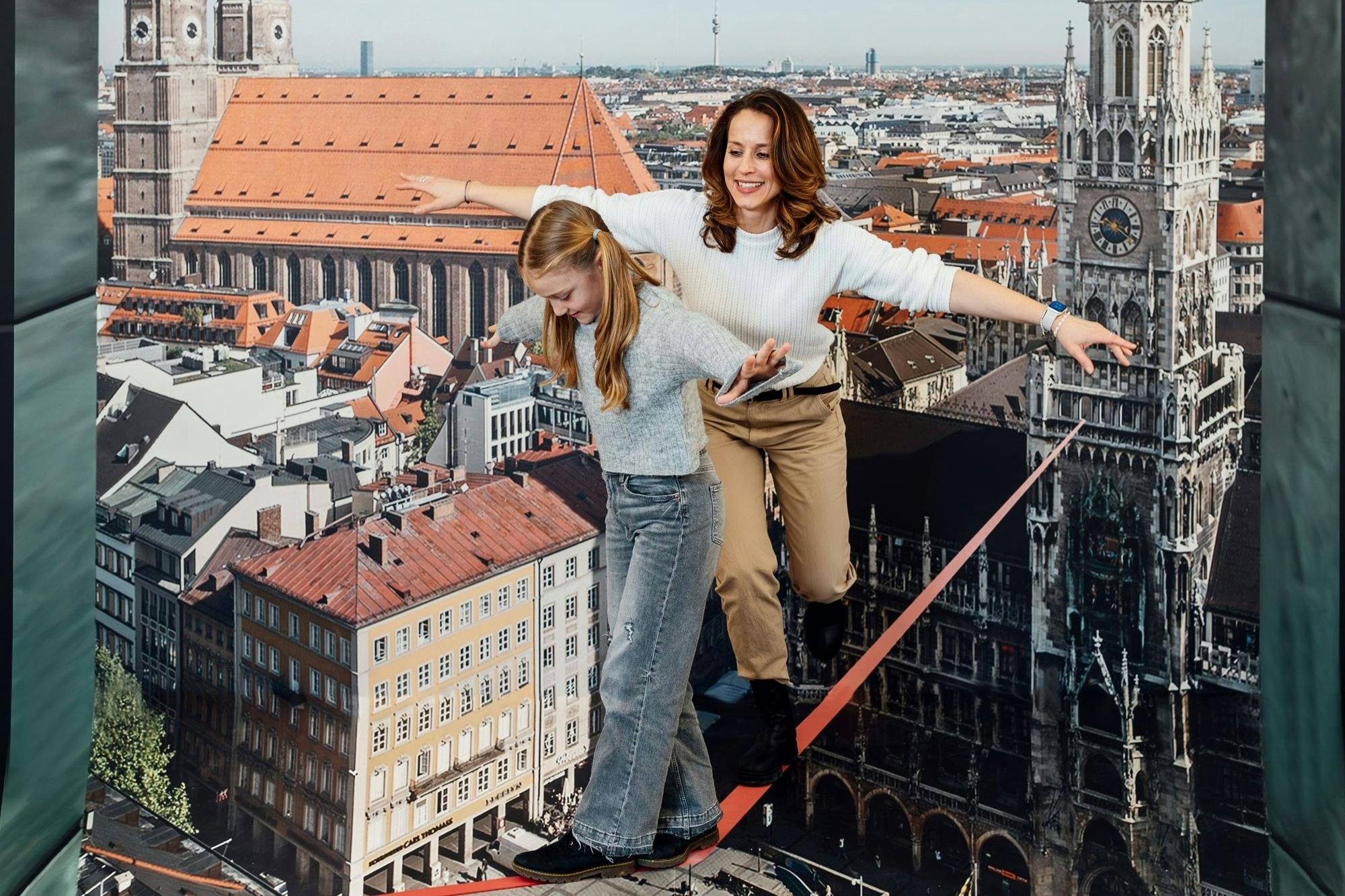 ミュンヘンの屋根の上のスラックラインでバランスをとる母親と娘–マジックバイエルンのスリル満点の錯覚。
