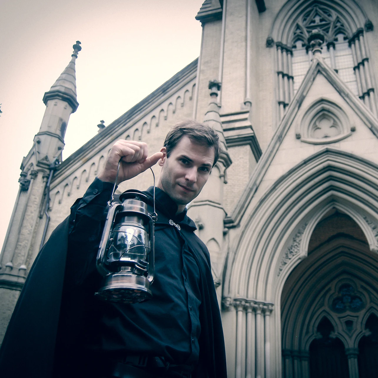 Man holding a lantern in front of a gothic-style building with arched windows and ornate detailing.