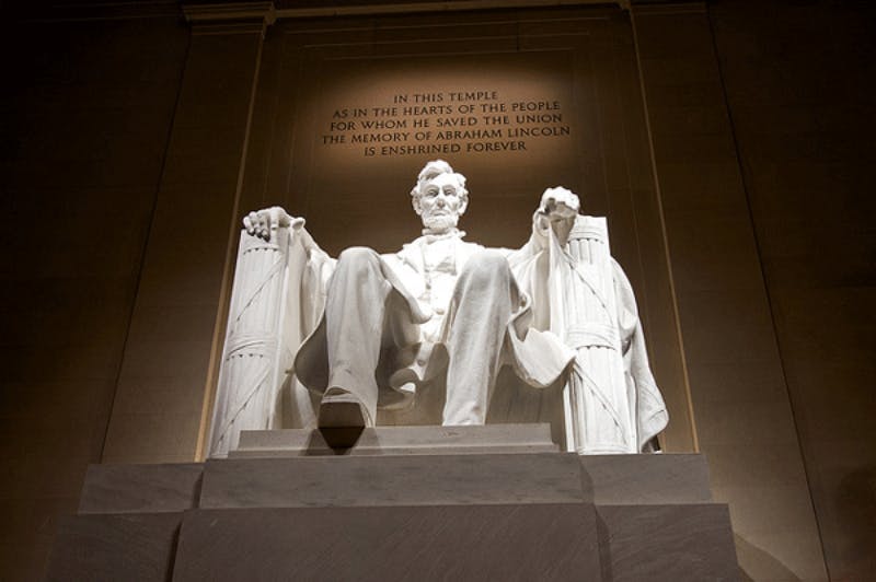Staty av Abraham Lincoln sittande i Lincoln Memorial med en inskription ovanför.