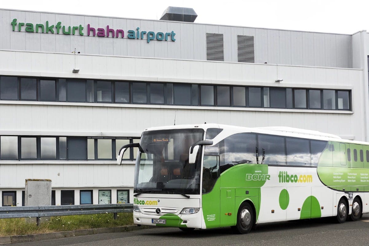 A green and white coach bus is parked in front of a building labeled "Frankfurt Hahn Airport."