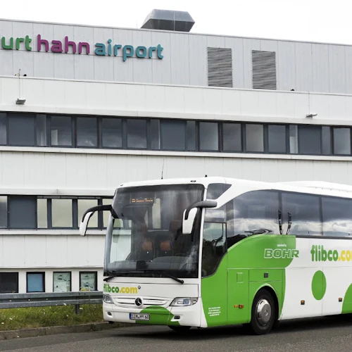 En grön och vit buss står parkerad framför en byggnad märkt "Frankfurt Hahn Airport".