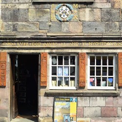 Stenhusfasad med krön, träsniderier och två fönster. ”John Knox House” skylt utanför en dörr.