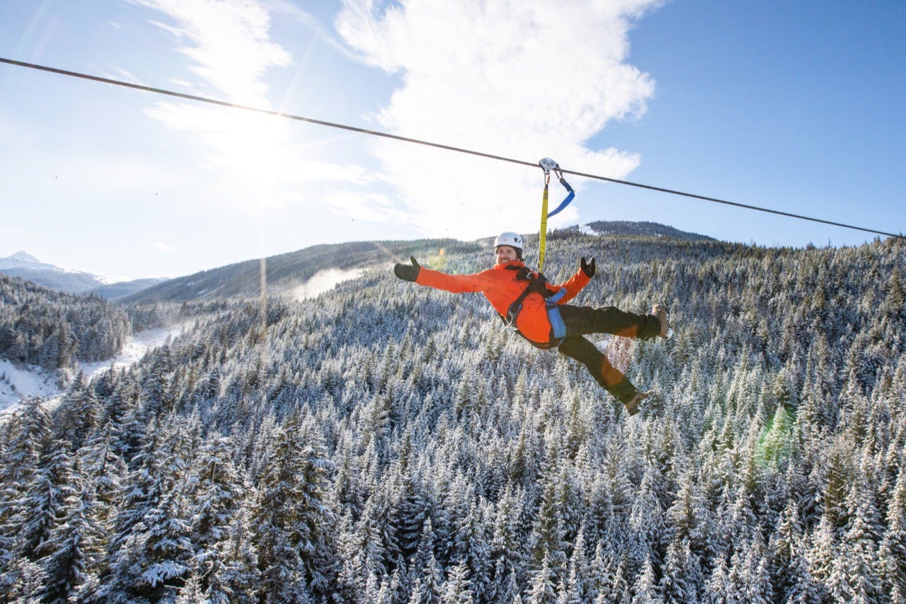 맑고 푸른 하늘 아래 눈 덮인 숲 속의 산 풍경 위에 밝은 주황색 재킷을 입은 사람.