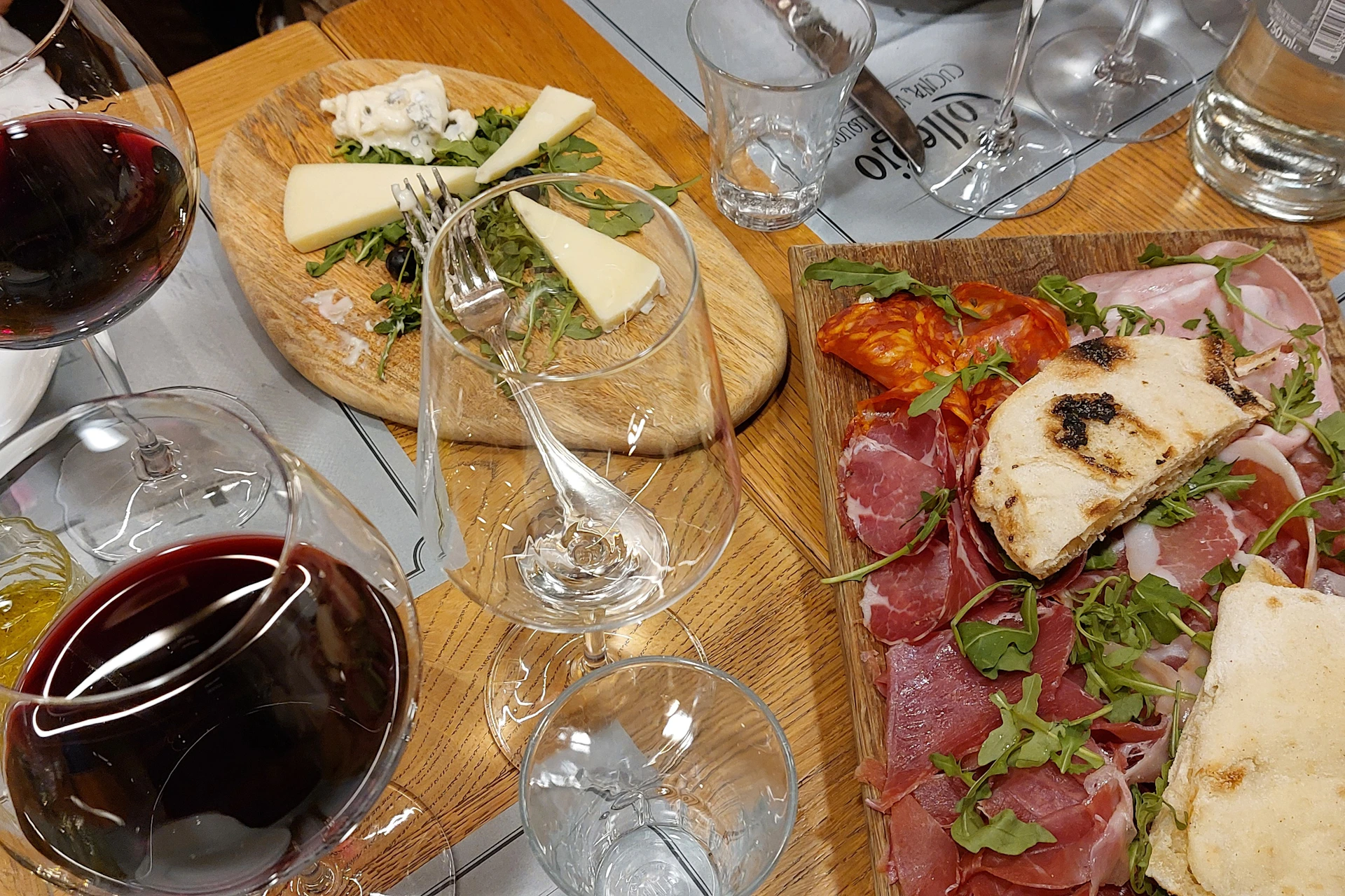 A charcuterie board with meats, cheese, arugula, and a glass of red wine on a wooden table.