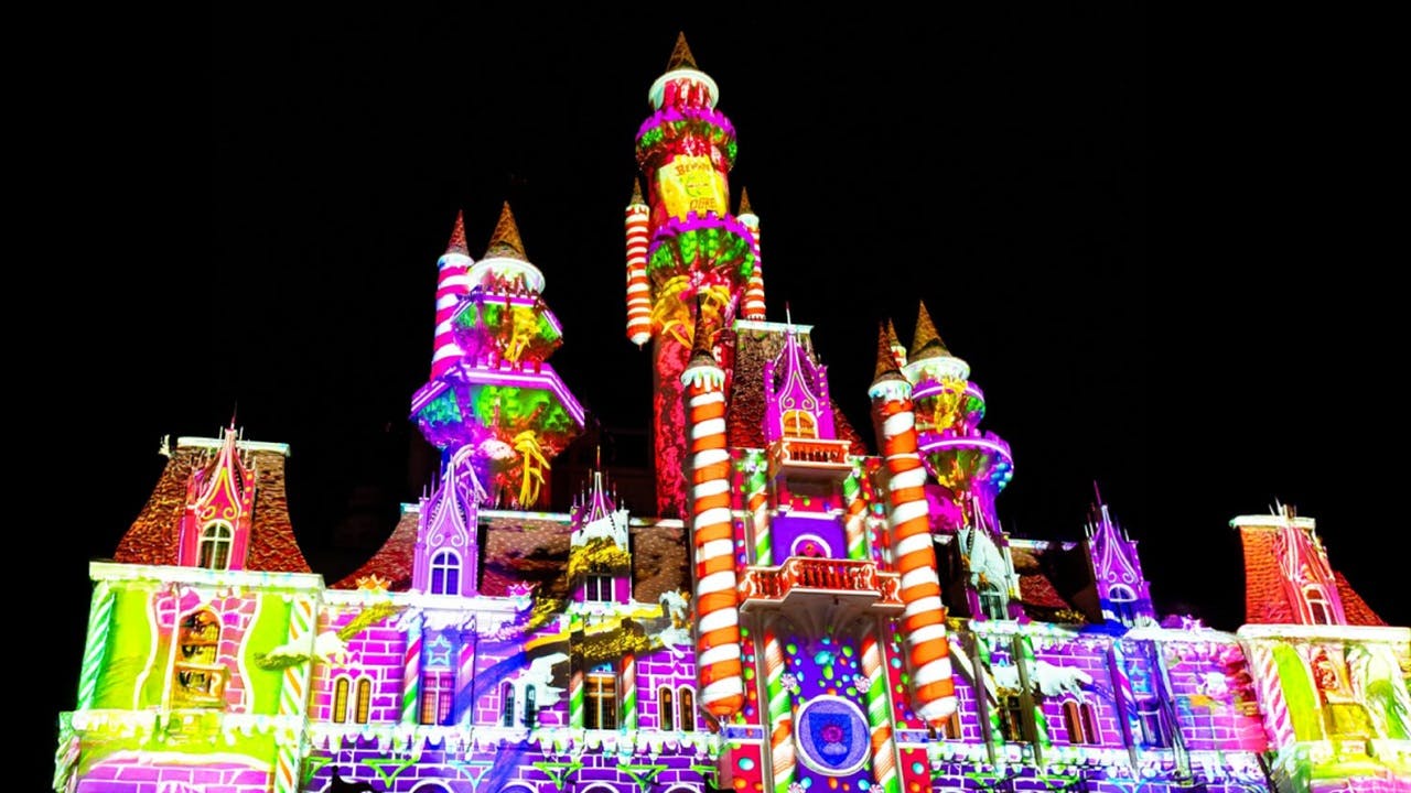 Zámek osvětlený živými barevnými projekcemi včetně pruhů cukrové třtiny, vzorů a různých slavnostních vzorů v noci.