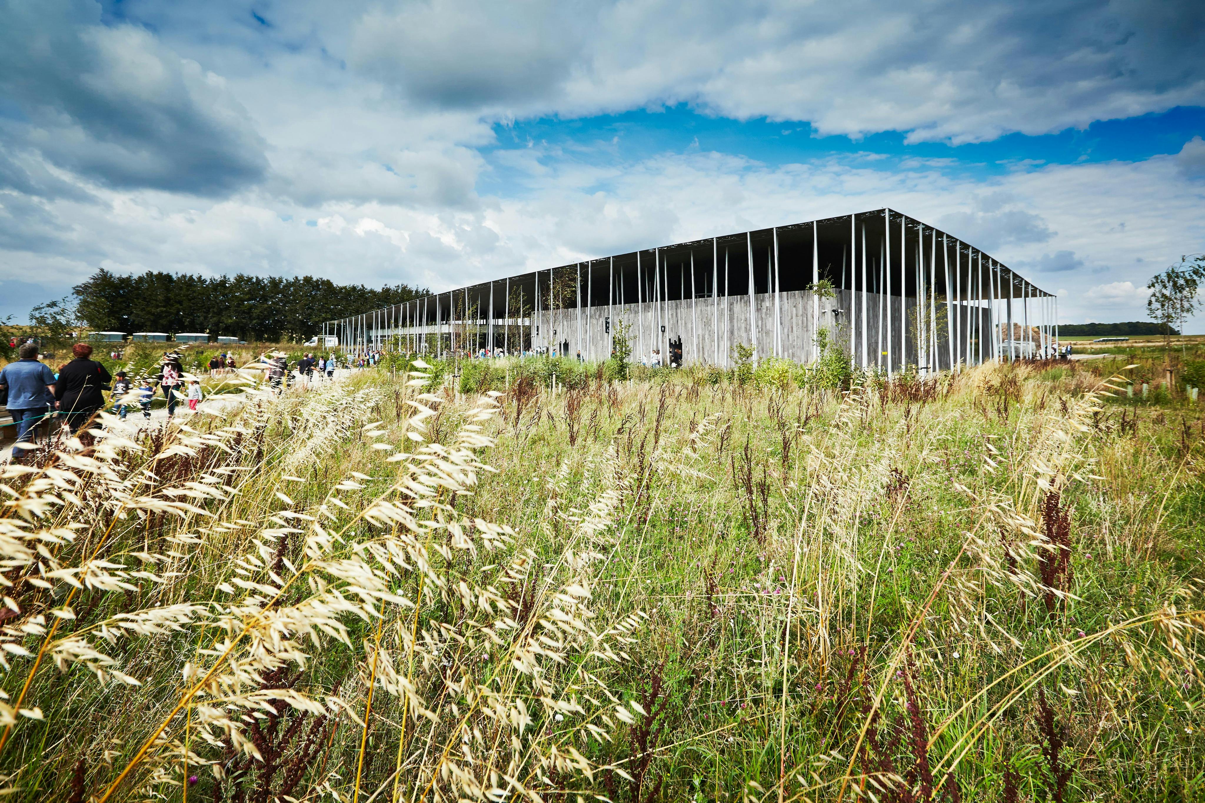 A modern building with vertical slats surrounded by tall grass under a partly cloudy sky.