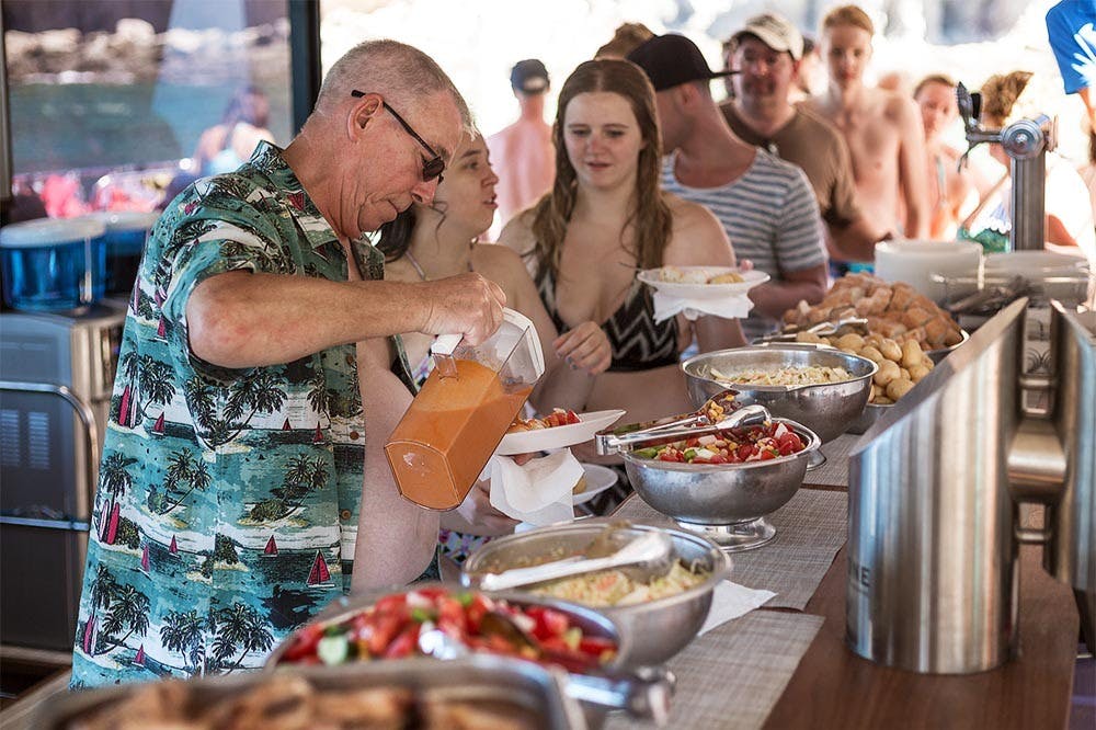 一群穿着泳装的人正在为自己提供各种菜肴和饮品分配器的自助餐。
