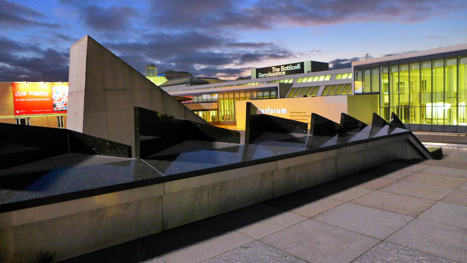 Modern buildings with sharp angles and dark reflecting surfaces, with a sign for "The Botticelli Renaissance" exhibit.
