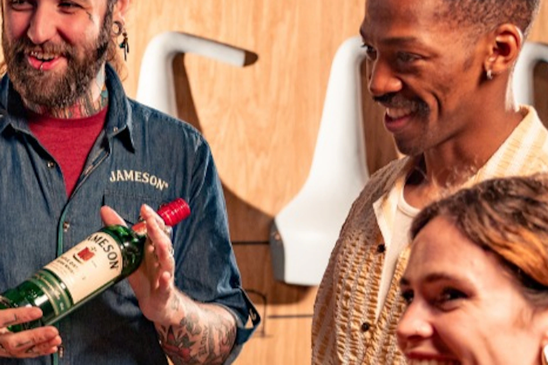 A group of people enjoying a whiskey-tasting session at a distillery, with a presenter holding a bottle of Jameson.
