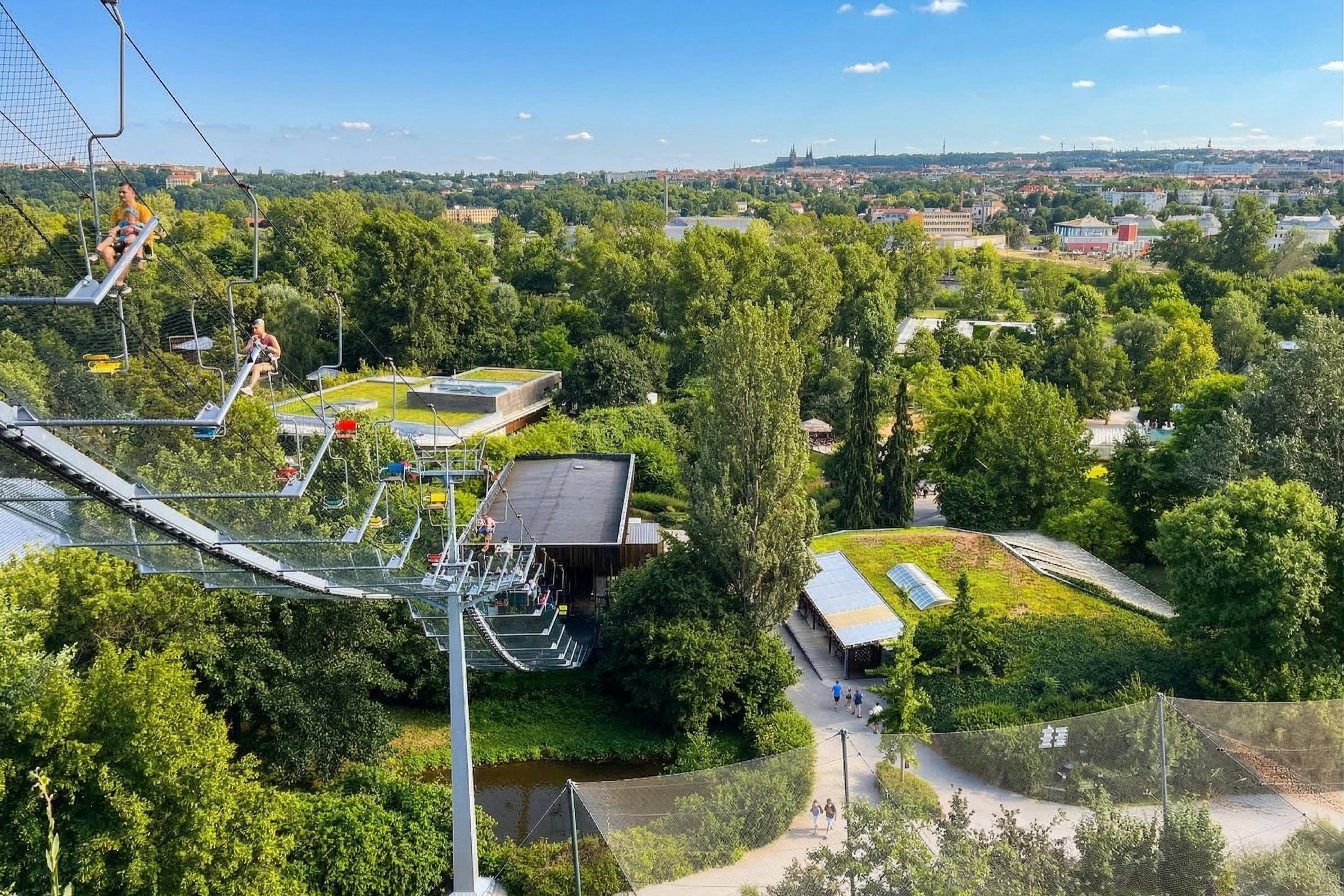 En smuk udsigt over en park med træer, en zip line-tur og folk, der går på stier under en klar blå himmel.