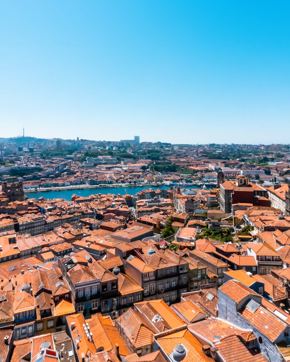Aerial view of a city with numerous terracotta-roofed buildings, a river running through the center, and a clear blue sky.