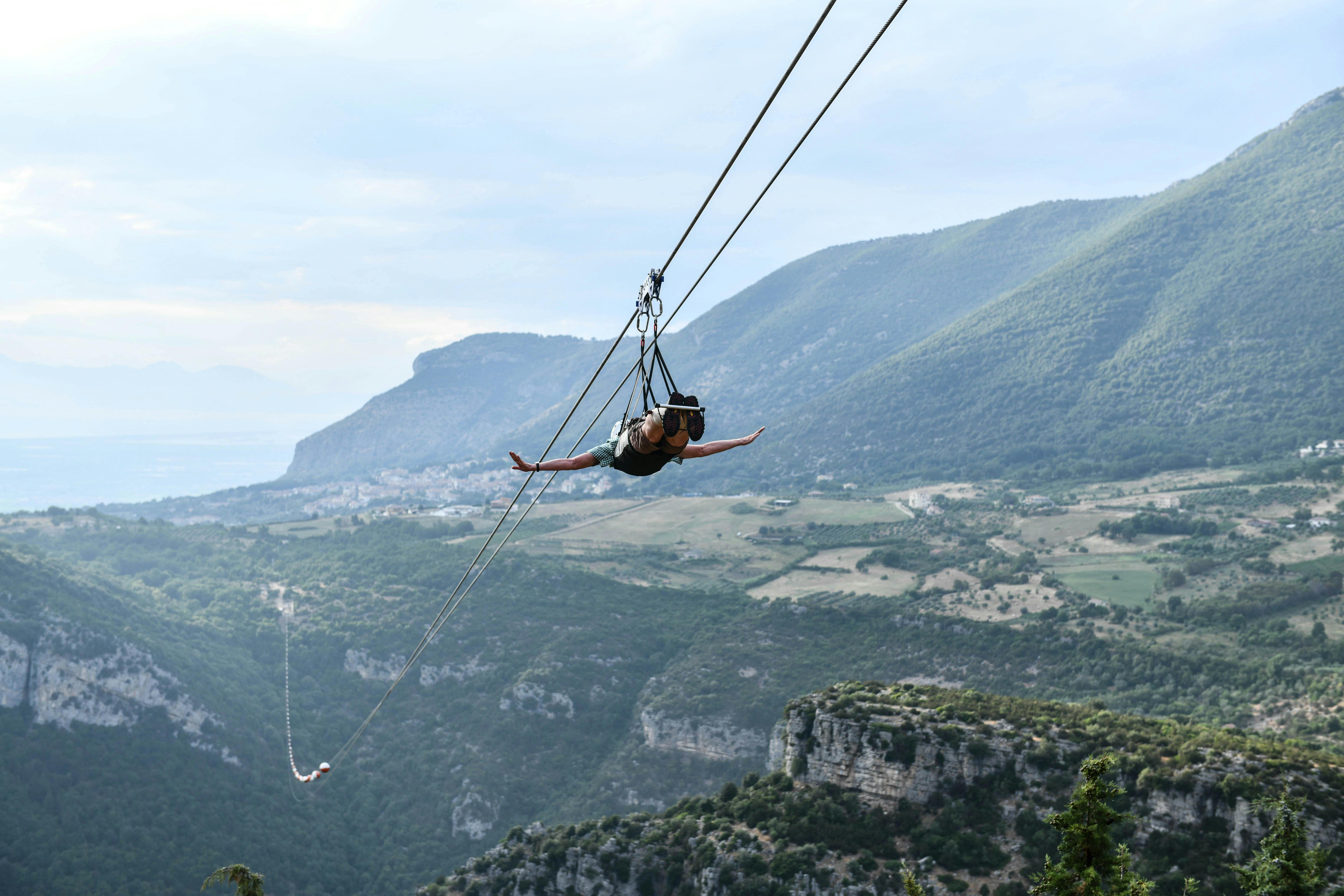 在一片多云的天空下，人工拉链穿过风景优美的山地景观，山谷和绿意盎然。