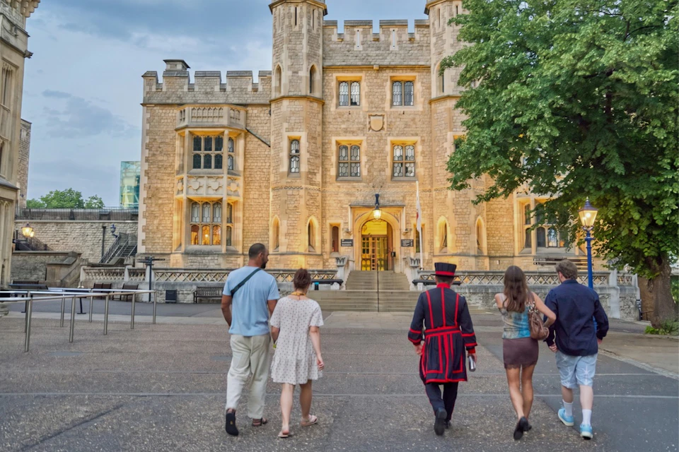 A group of people walking towards a historic castle entrance, with one person dressed in traditional ceremonial attire.