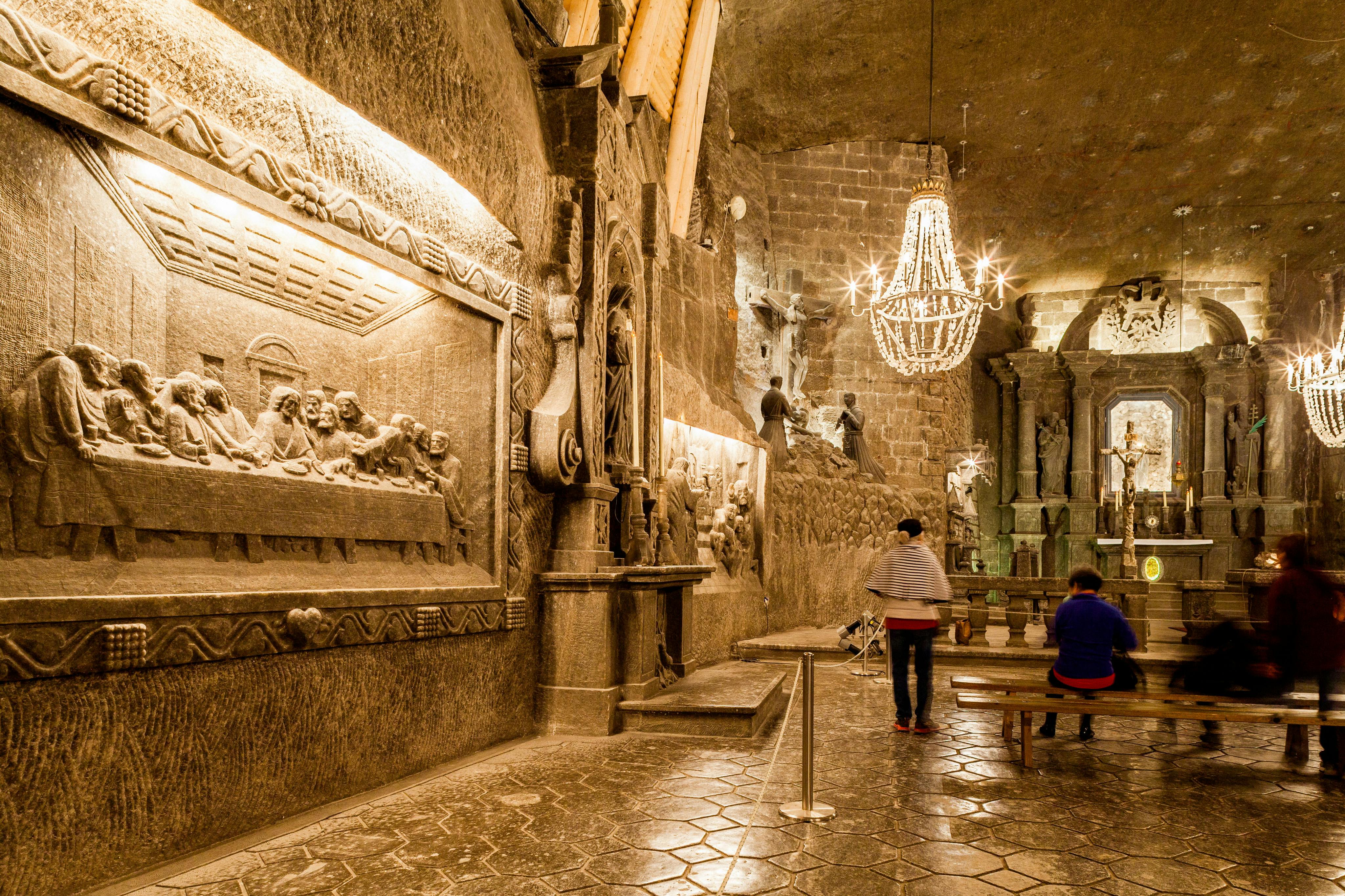 A room with intricately carved stone walls, a chandelier, and two people observing the artwork.