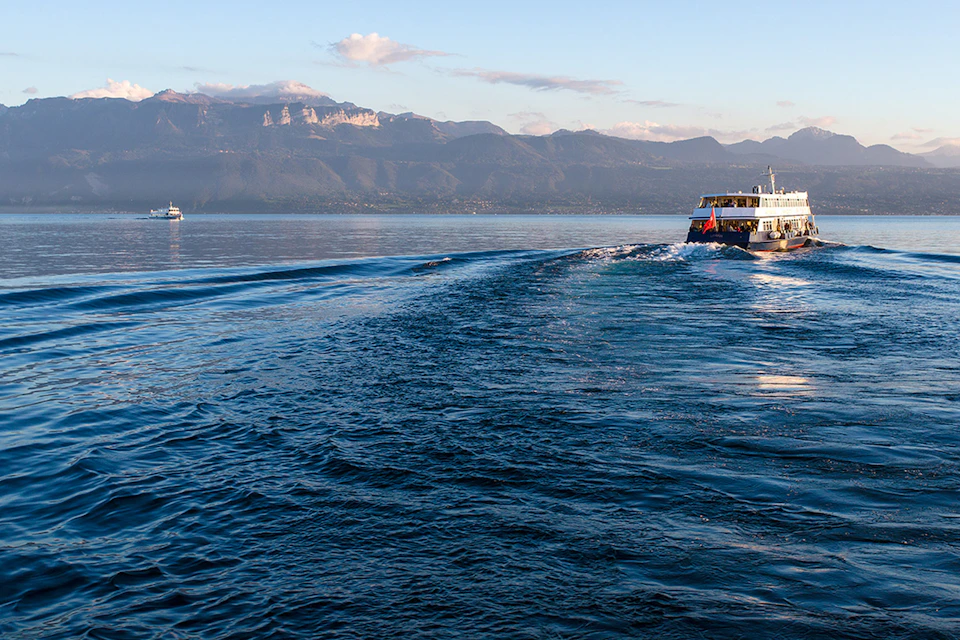 A boat sails on a calm lake with mountains in the background under a partly cloudy sky.