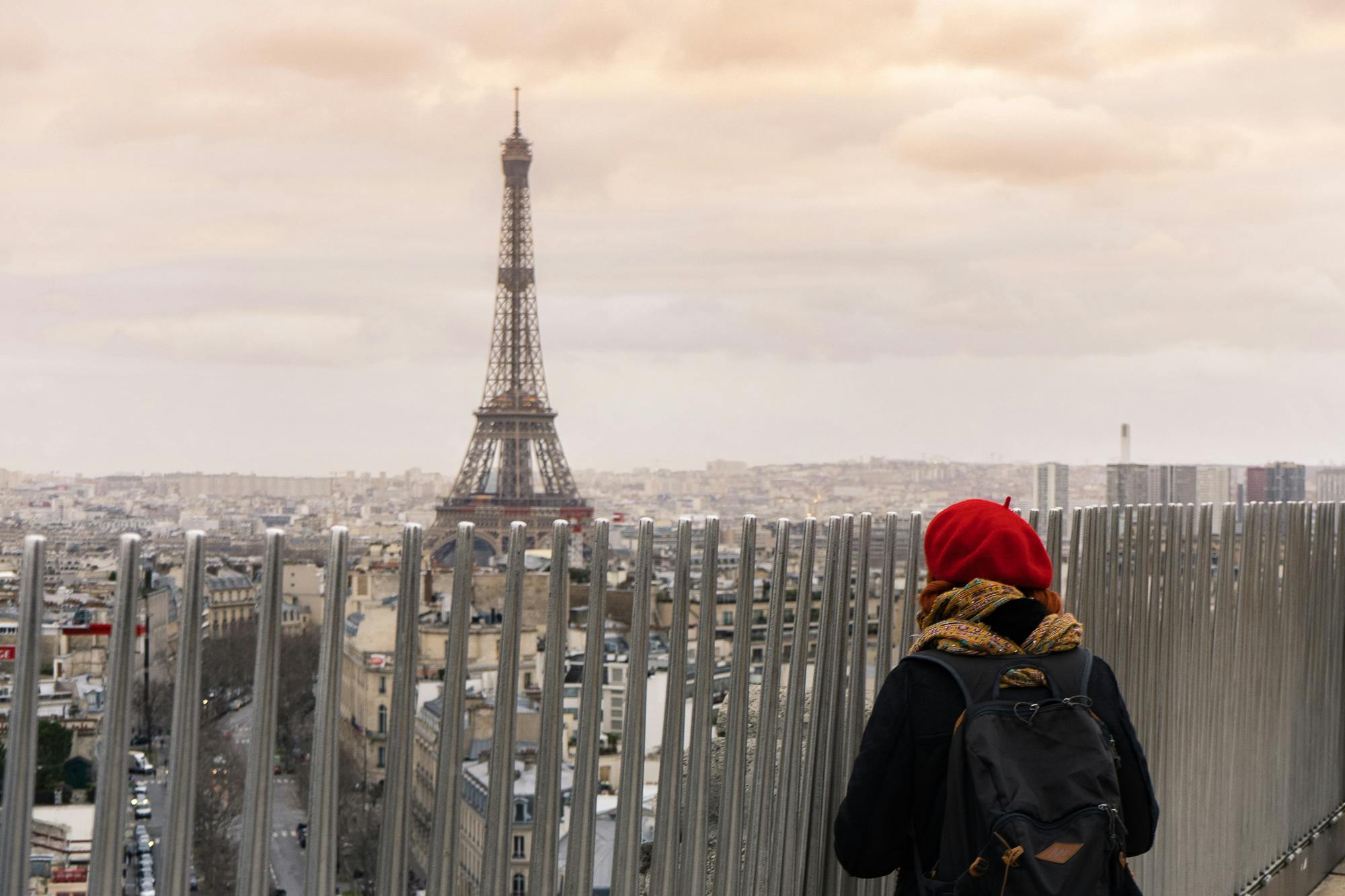 Woman in red beret looks at the Eiffel Tower from atop the Arc de Triomphe.