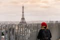 Vrouw met rode baret kijkt naar de Eiffeltoren vanaf de top van de Arc de Triomphe.