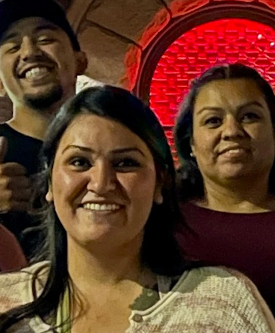 A group of people posing in front of a lit-up brick building at night, some wearing winter hats, smiling for the camera.
