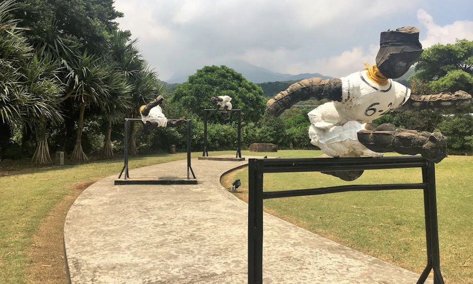 Outdoor display of goat sculptures mounted on metal frames along a path, surrounded by greenery and trees.