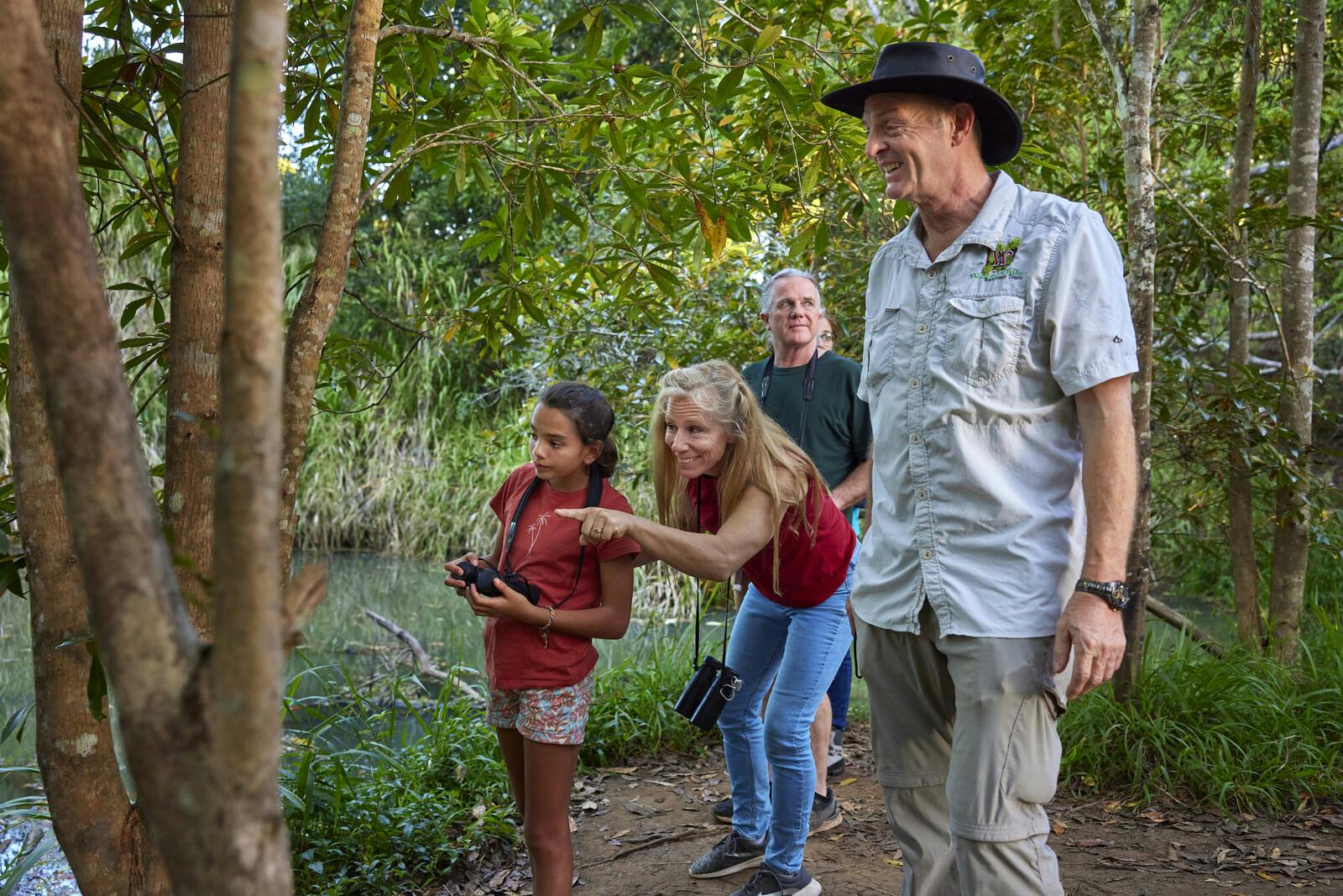 双眼鏡を持った少女、指さしている女性、そして水辺の森の土の小道に立っている2人の男性。