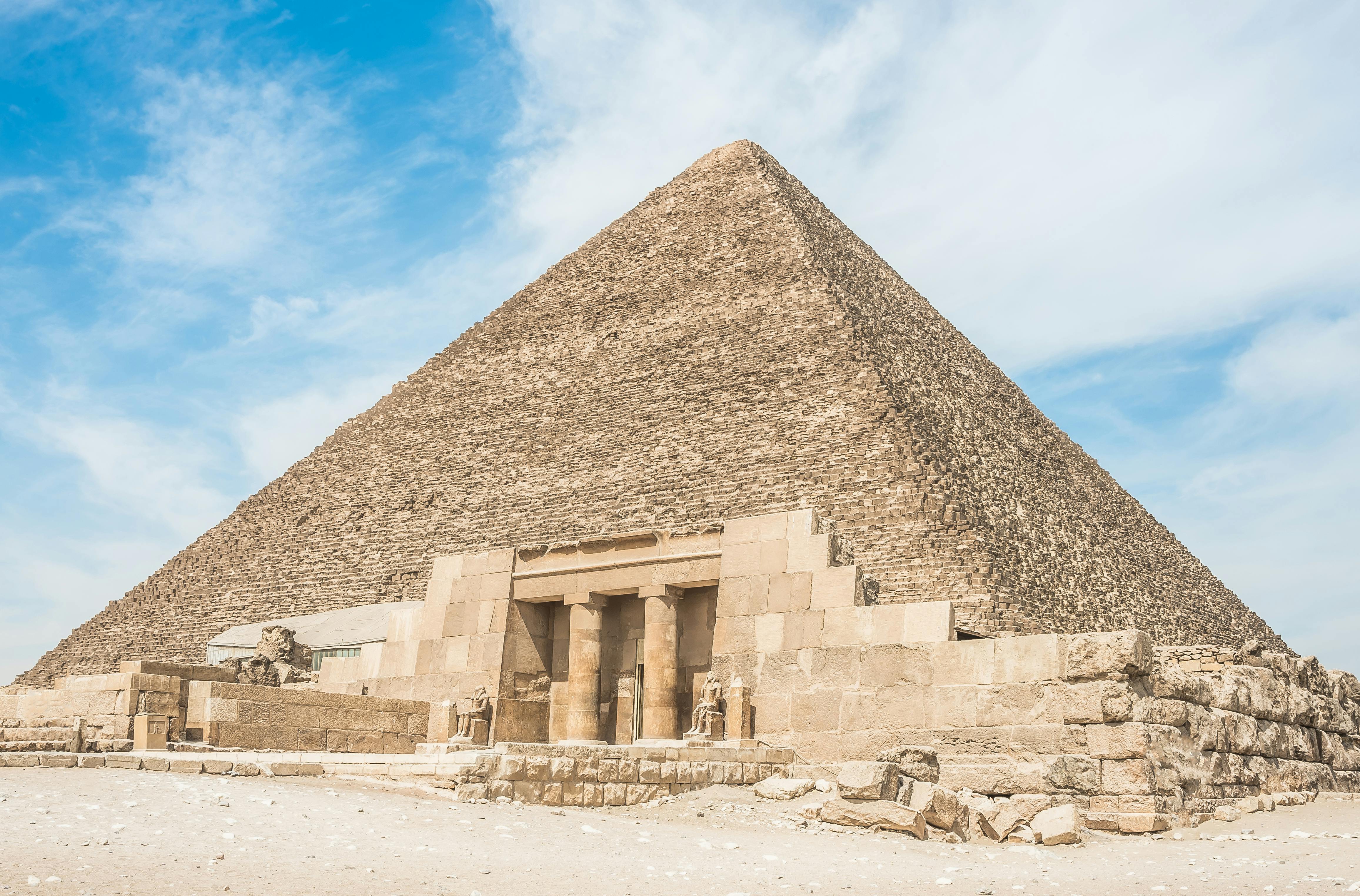 A large stone pyramid with an entrance flanked by statues under a clear blue sky.