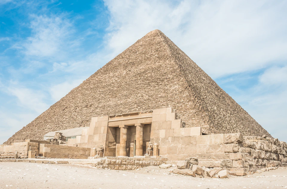 A large stone pyramid with an entrance flanked by statues under a clear blue sky.