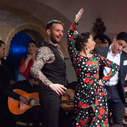 Utövare i livlig klädsel deltar i en livlig flamencodans, uppbackad av musiker som spelar gitarrer i en intim miljö.