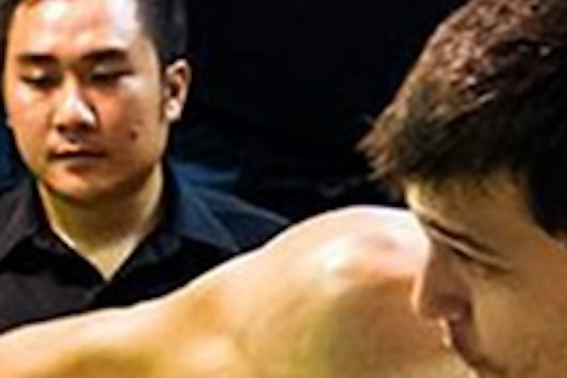 A Muay Thai match in a boxing ring, showing one fighter kicking and another dodging. A referee is observing in the background.