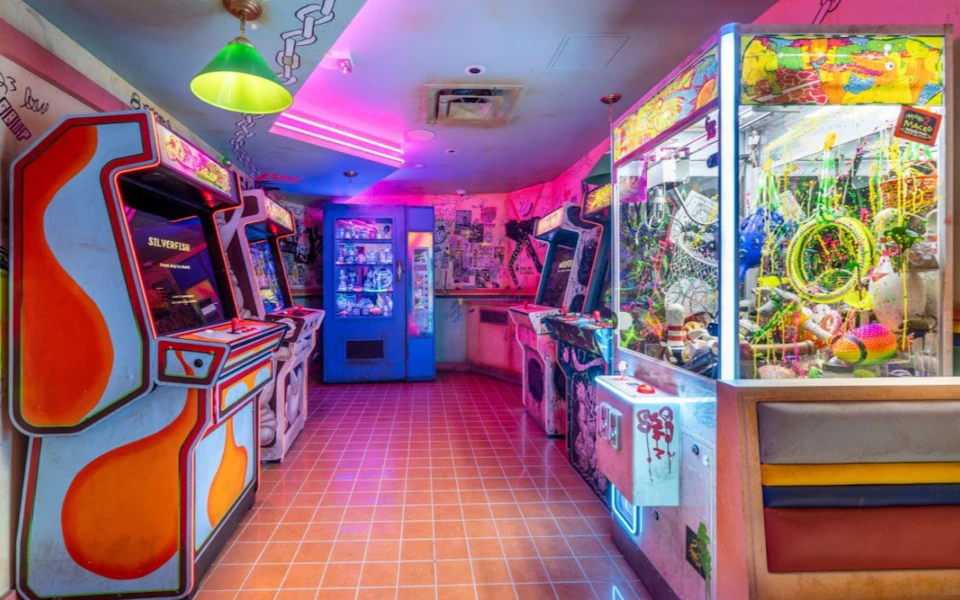 A colorful arcade room with various game machines, a vending machine, and neon lighting on the walls and ceiling.
