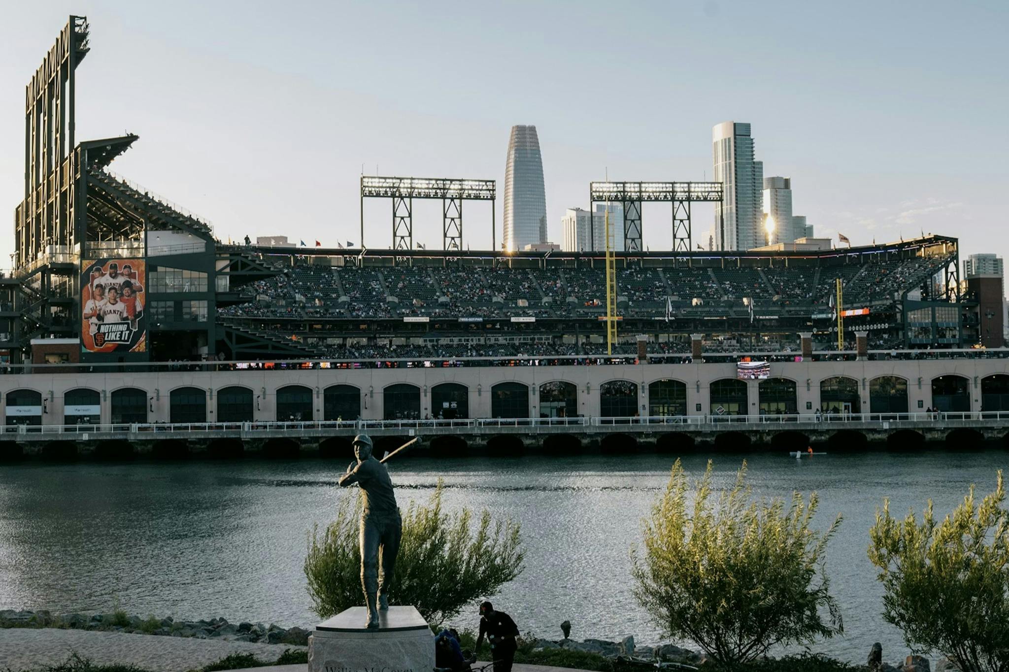 Nábřežní baseballový stadion se sochou v popředí a městskými mrakodrapy v pozadí.
