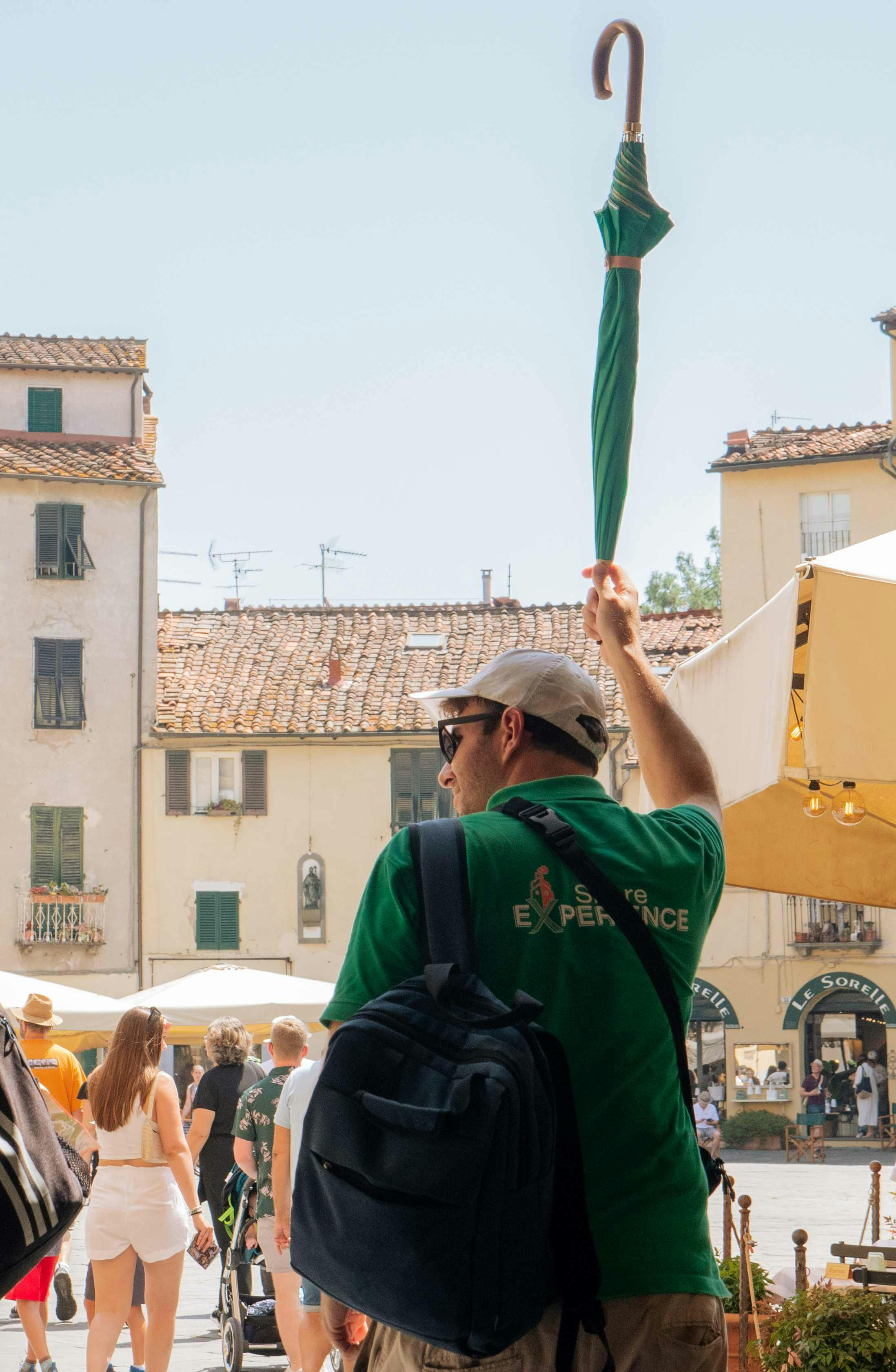 A man in a green shirt holds up an umbrella in a European square with old buildings and people walking around.
