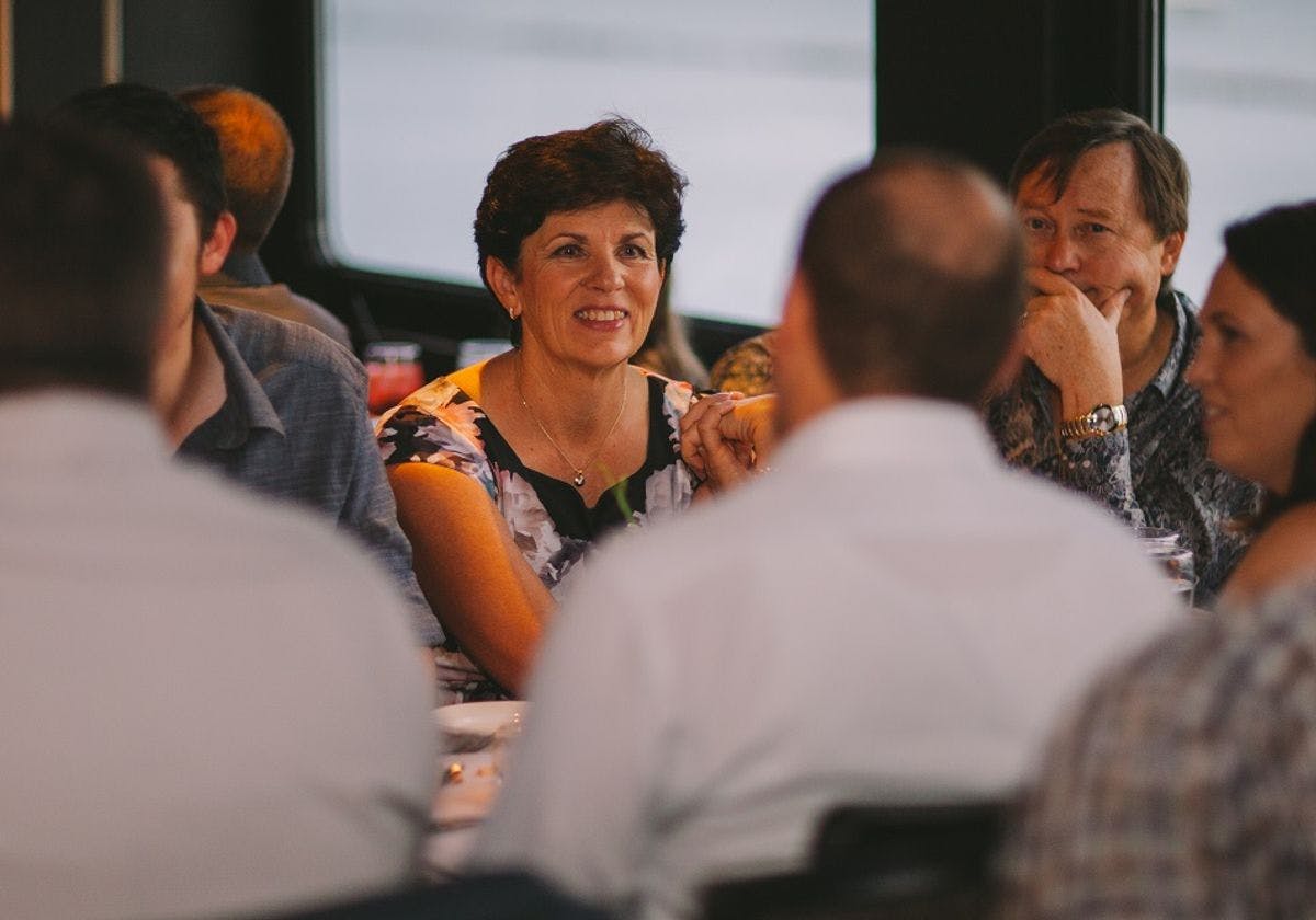 Four people sit around a table in conversation, three are visible, including a smiling woman and two men.