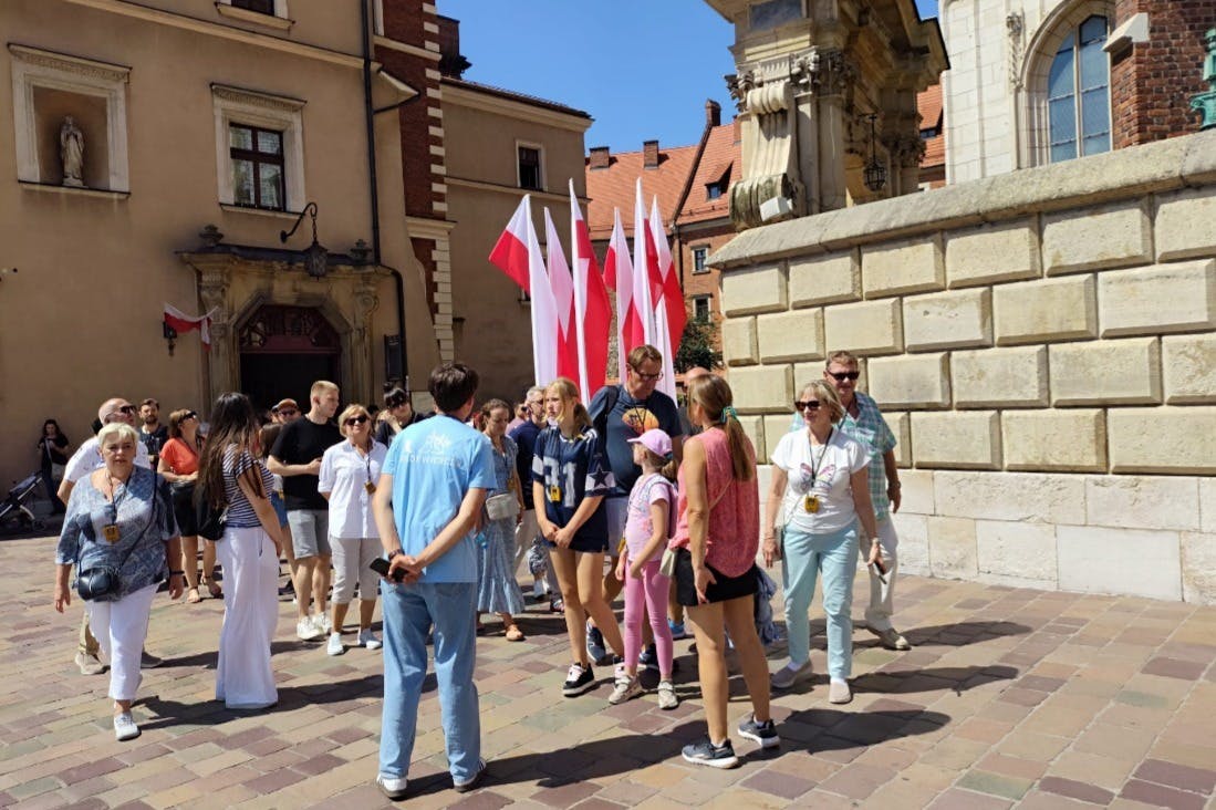 A group of people gathered in a town square with a building and multiple flags in the background on a sunny day.