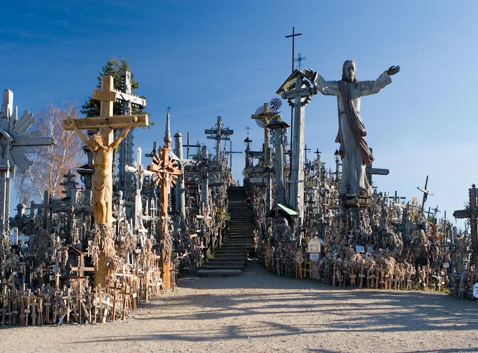 A hillside filled with numerous crosses, a large statue of Jesus with open arms, and a clear blue sky in the background.