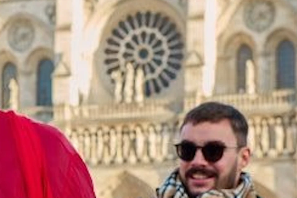 A group of people near Notre-Dame Cathedral in Paris, one wearing a red jacket with 'Paris City Vision' branding.