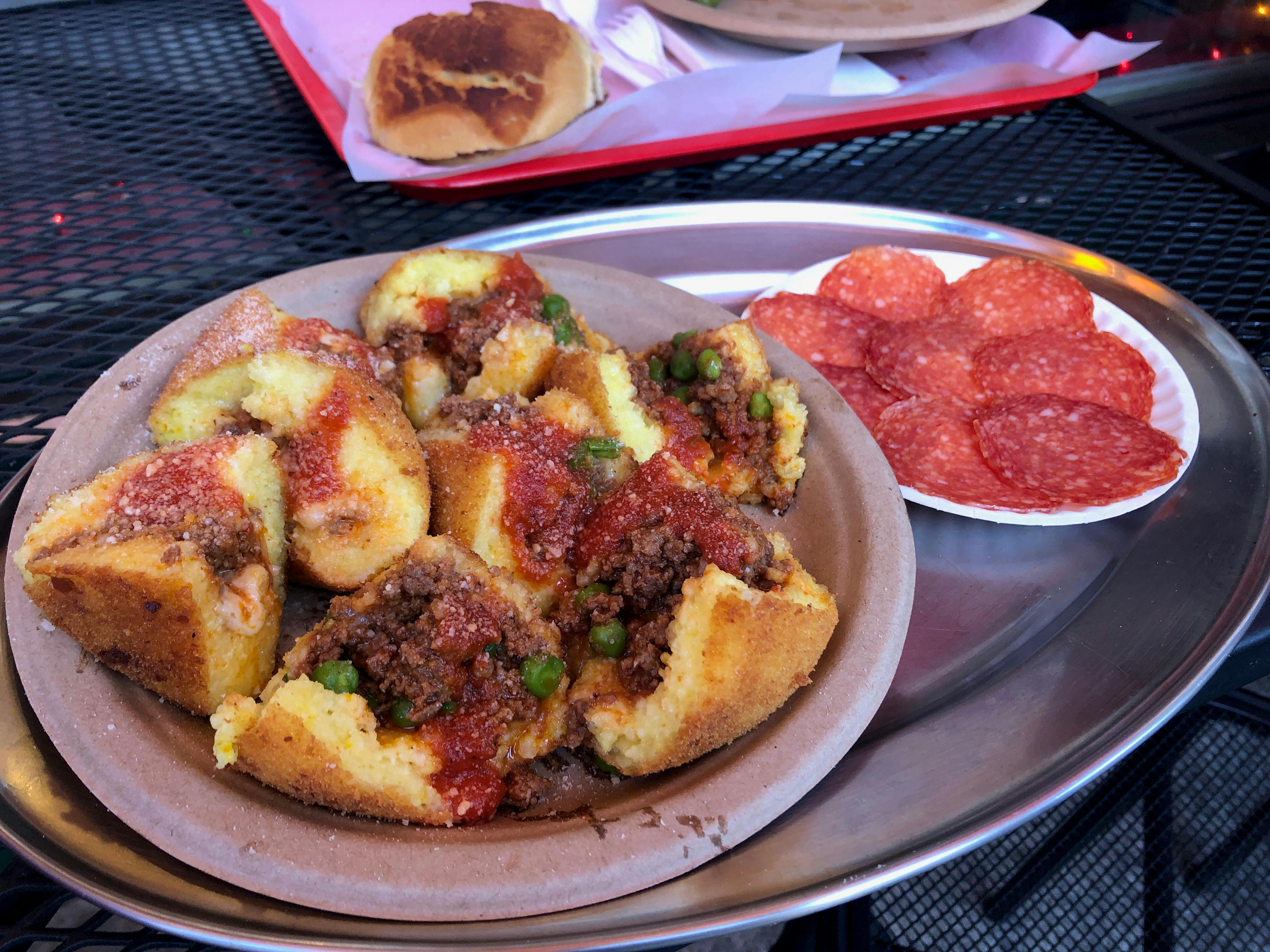 Plate of stuffed polenta with meat and peas, garnished with tomato sauce. Side dish of sliced pepperoni on the same tray.