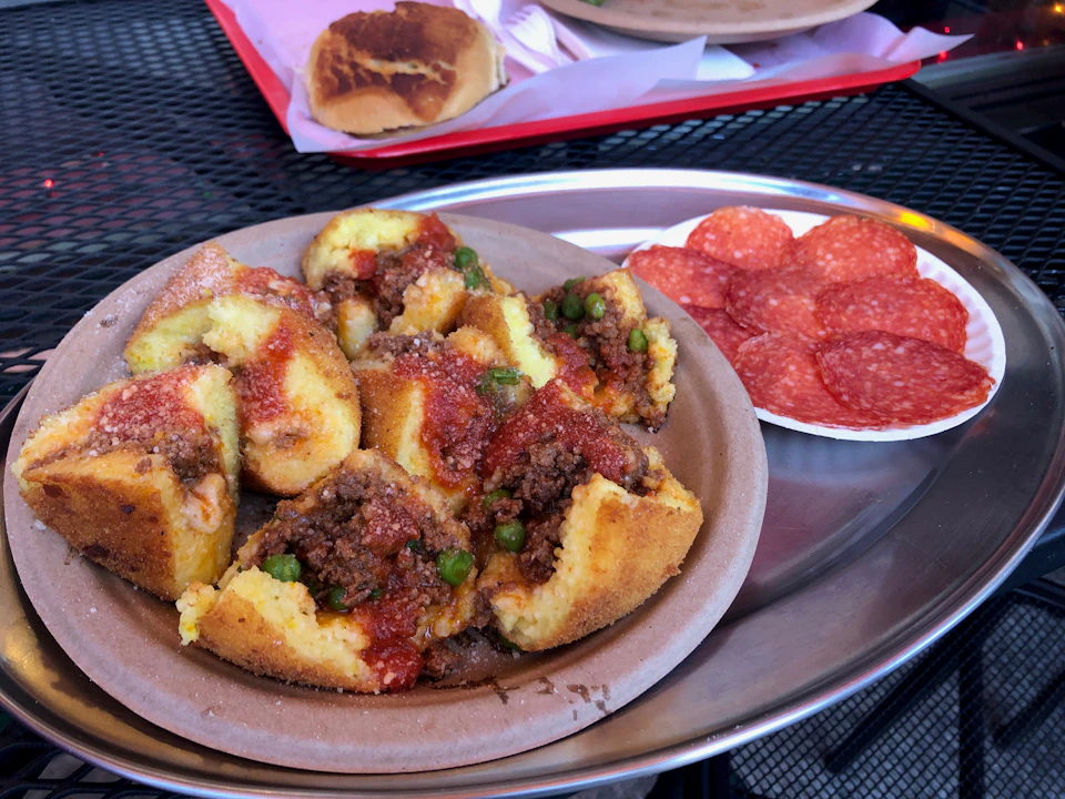 Plate of stuffed polenta with meat and peas, garnished with tomato sauce. Side dish of sliced pepperoni on the same tray.
